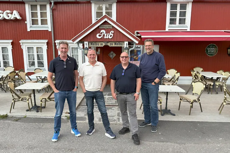 Fire medlemmer av Leca Infra-teamet står foran en rød pubbygning i Melbu sentrum, klare for prosjektreise i nord.