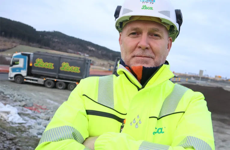 Frank Nornberg fra Leca i gul refleksjakke og hjelm foran anleggsområdet ved Leistadkrysset, med Leca-lastebil i bakgrunnen.