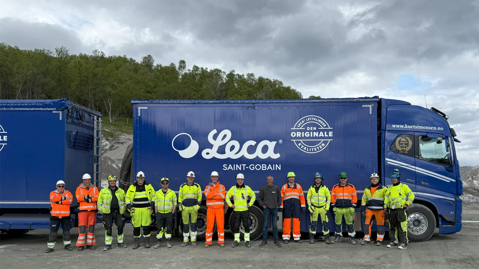 Infra-teamet og samarbeidspartnere poserer foran to store blå Leca-blåsebiler på riggområdet utenfor tunnelen