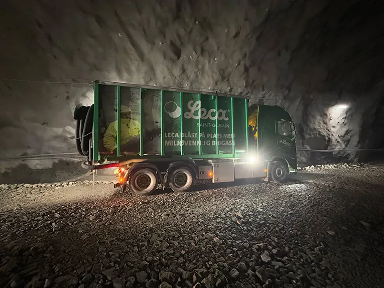 Grønn Leca-lastebil inne i Hestnestunellen under leveranse av Leca® Lettklinker. Bilen er merket med teksten «LECA BLÅST PÅ PLASS MED MILJØVENNLIG BIOGASS» og står parkert i det mørke tunellrommet med lys som lyser opp området.