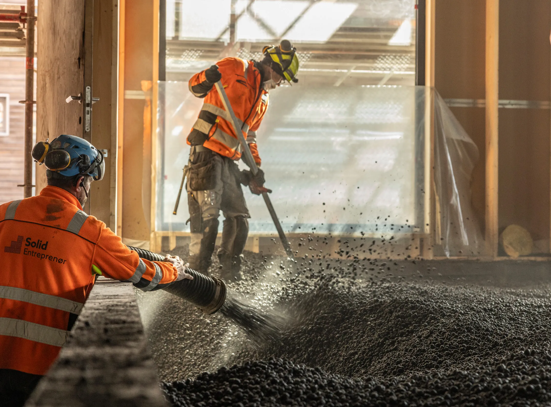 To arbeidere legger ut Leca lettklinker inne i et bygg for isolasjon og oppfylling.