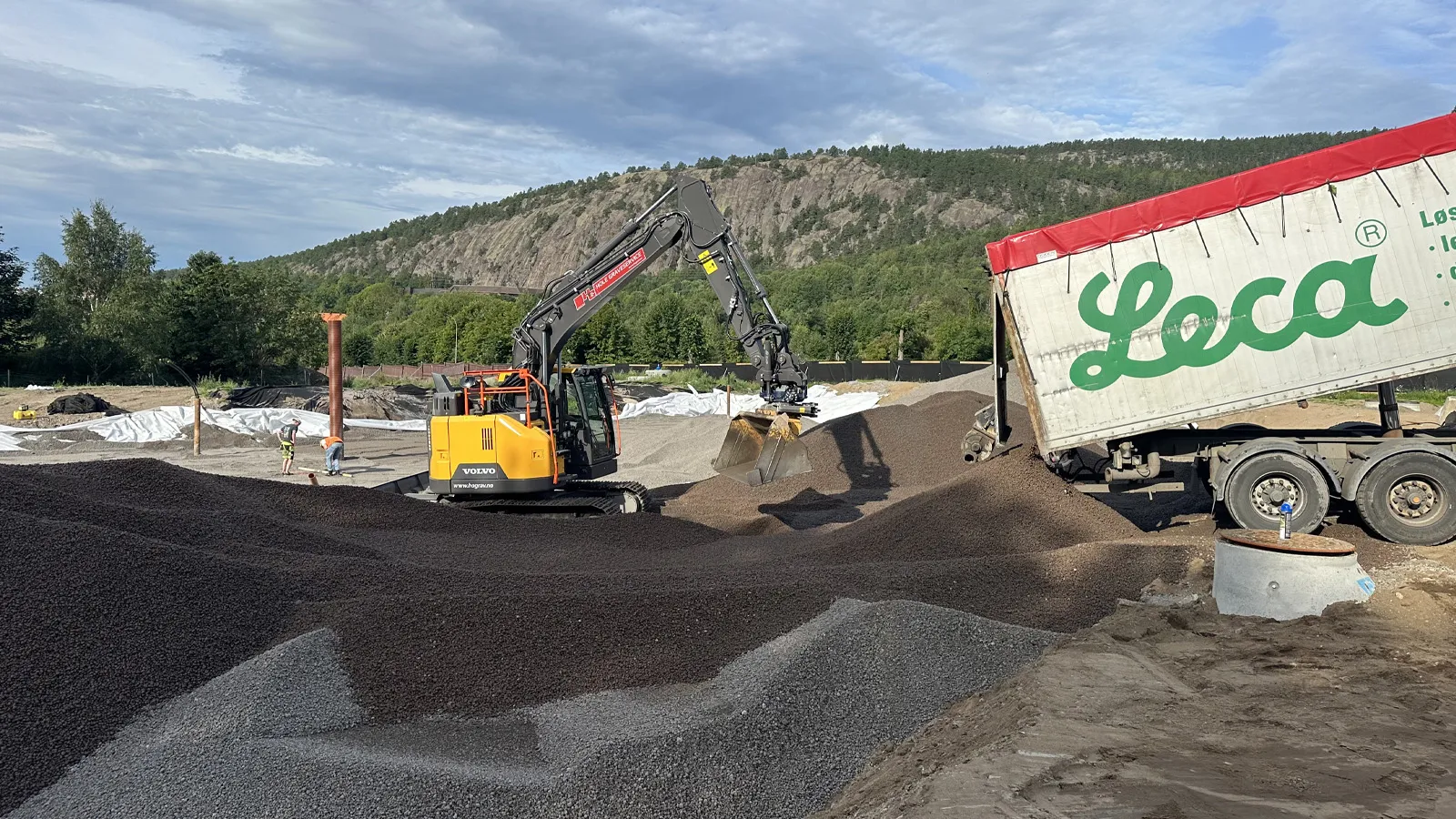 Leca-bil tømmer lettklinker på tomta for Tofte brannstasjon mens maskin fordeler massene