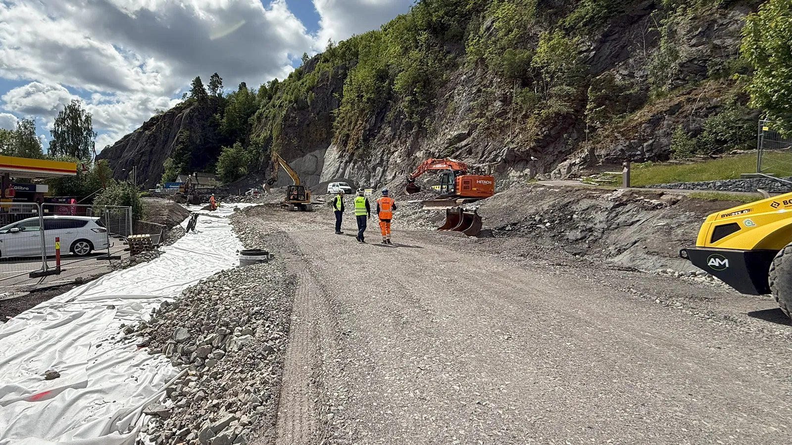 Oversiktsbilde av anleggsområdet i Holmestrand sentrum med utlegging av masser og synlig geotekstil, gravemaskiner i arbeid langs fjellskjæring.
