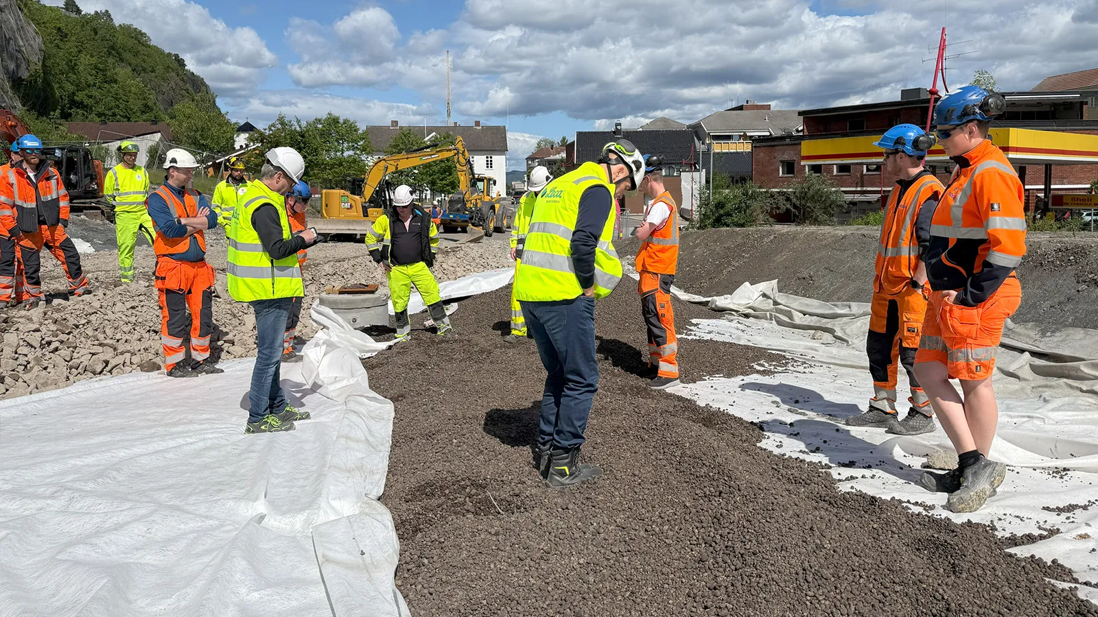 Gruppe med ingeniører og anleggsarbeidere fra Leca, Isachsen og Norconsult inspiserer utlagt Leca® Lettklinker på byggeplass i Holmestrand sentrum. Personene står på geotekstil med lettklinker og steinmasser rundt seg.