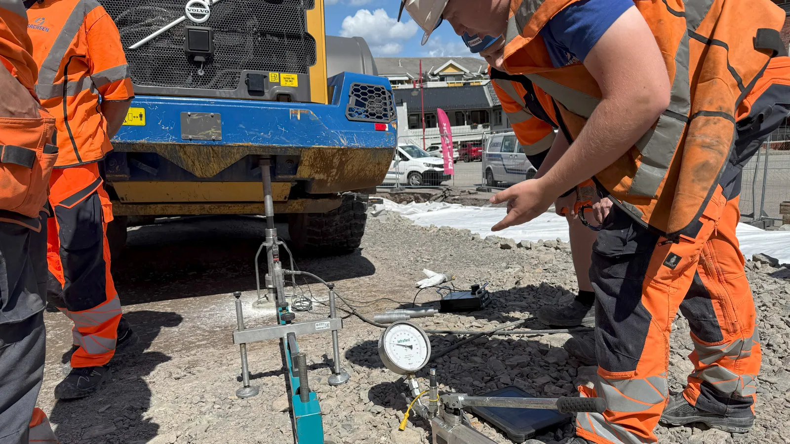 Nærbilde av anleggsarbeidere som gjennomfører platetesting for kontroll av setninger i grunnen foran en stor maskin.