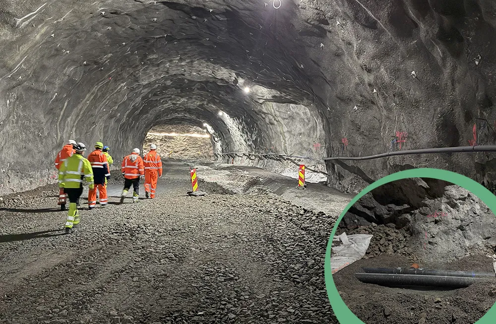 Arbeidere i sikkerhetsutstyr går gjennom Gullesfjordtunnelen under bygging, med synlig vann- og avløpsrør i innsvinget markert i hjørne. Tunnelveggen er uarmert fjell, og underlaget består av grovpukk og Leca Lettklinker.