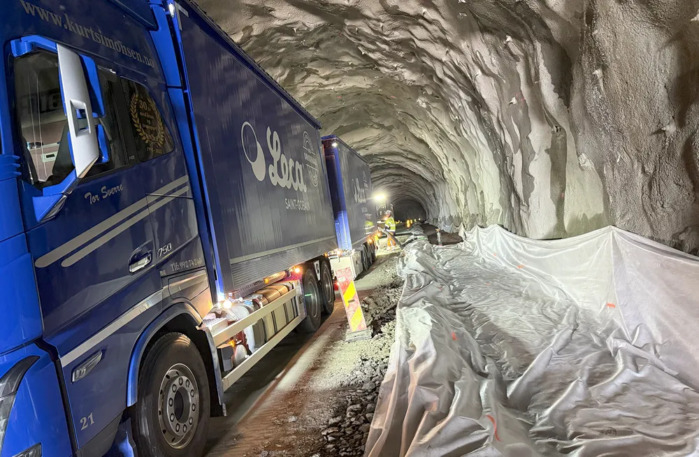 Leca-blåsebil inne i tunnel på Hålogalandsvegen. Arbeidere klargjør grøft for isolering med lettklinker. Fiberduk er lagt klart langs tunnelløpet.