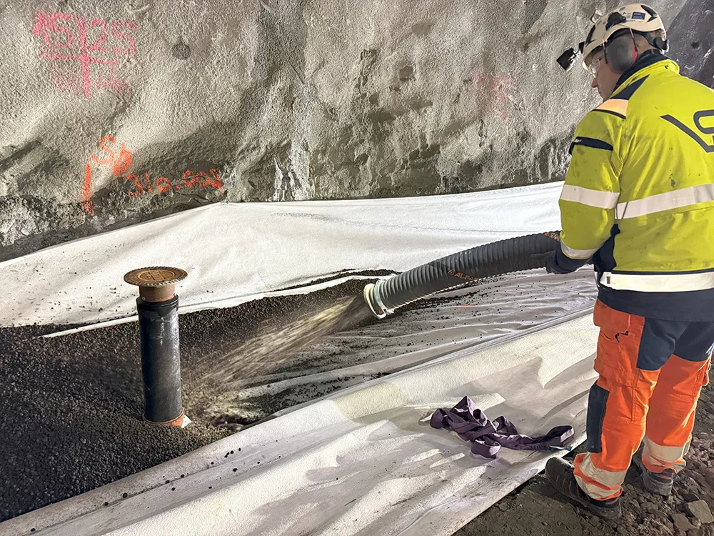 Arbeider med hjelm og hørselvern blåser Leca Lettklinker ned i en grøft dekket med fiberduk inne i tunnel.