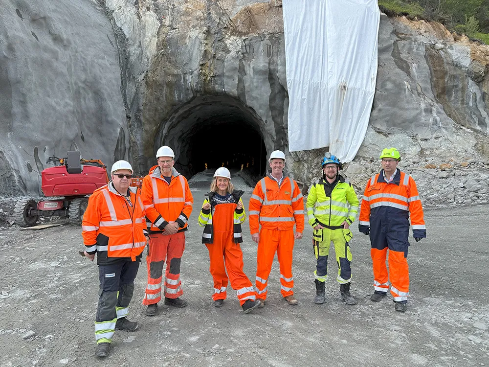 Leca-team og samarbeidspartnere poserer foran tunnelåpning ved Hålogalandsveien, med fjell og maskiner i bakgrunnen.