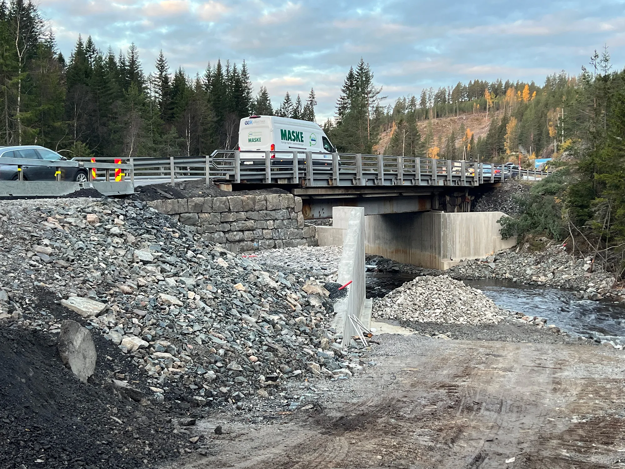 Kobbervoll bru på E134 etter utskifting. Kjøretøy passerer over brua, mens ny betongkonstruksjon og elveløp med steinfylling er synlig under. Skog og høstfarger i bakgrunnen.