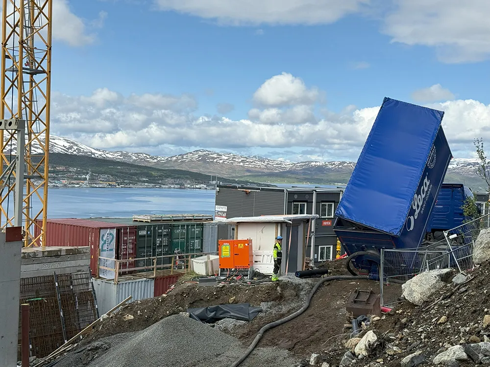Leca-blåsebil med åpen luke tømmer lettklinker inn på byggeplass i et boligområde i Kroken, med fjord og fjell i bakgrunnen