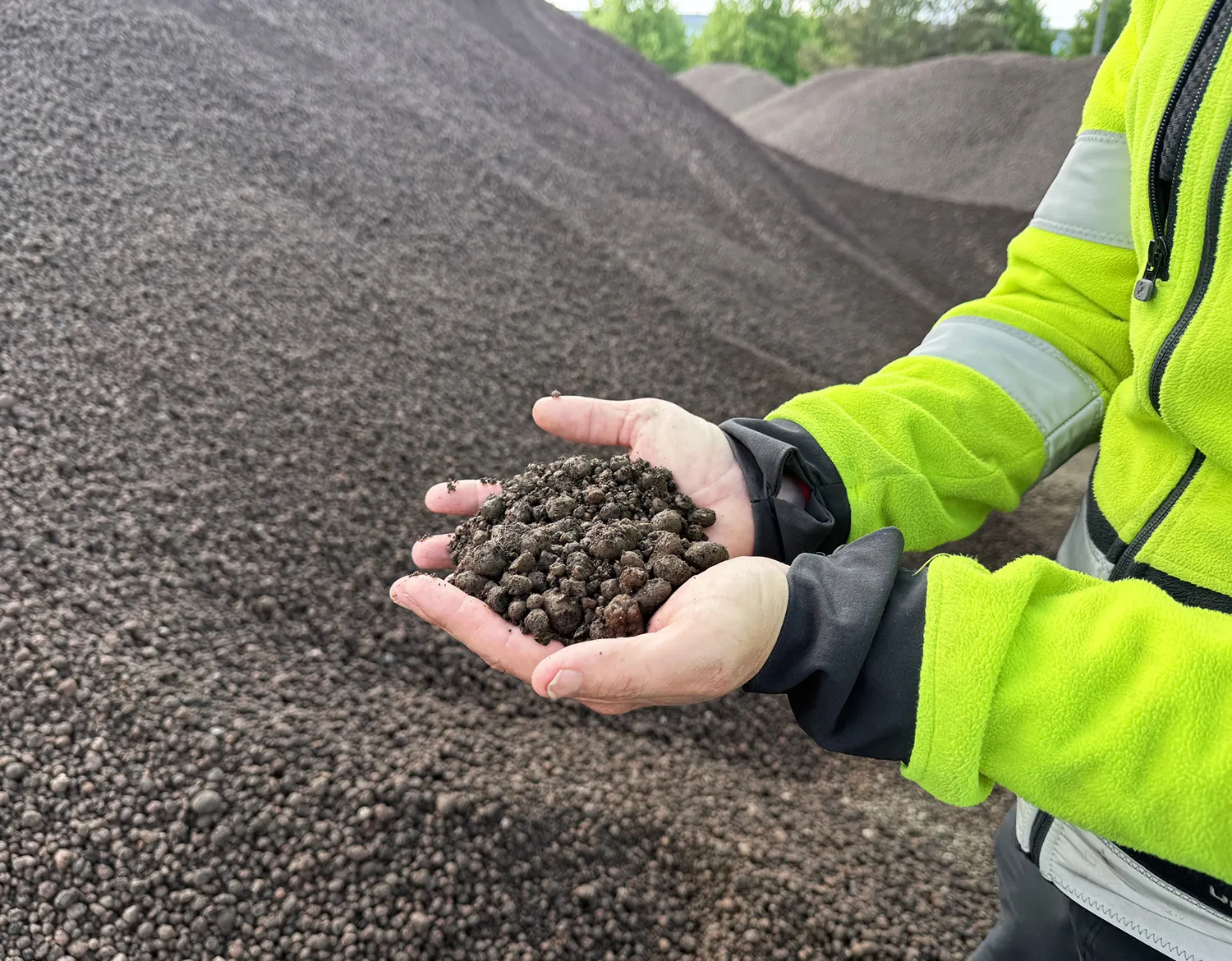 Gjenbrukt Leca® Lettklinker holdes i hendene foran store masselagre.
