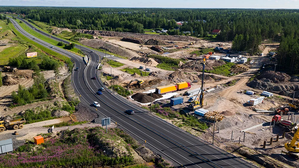 Flyfoto av veianlegg med nye og eksisterende veier, maskiner og byggeaktivitet i grønt landskap.