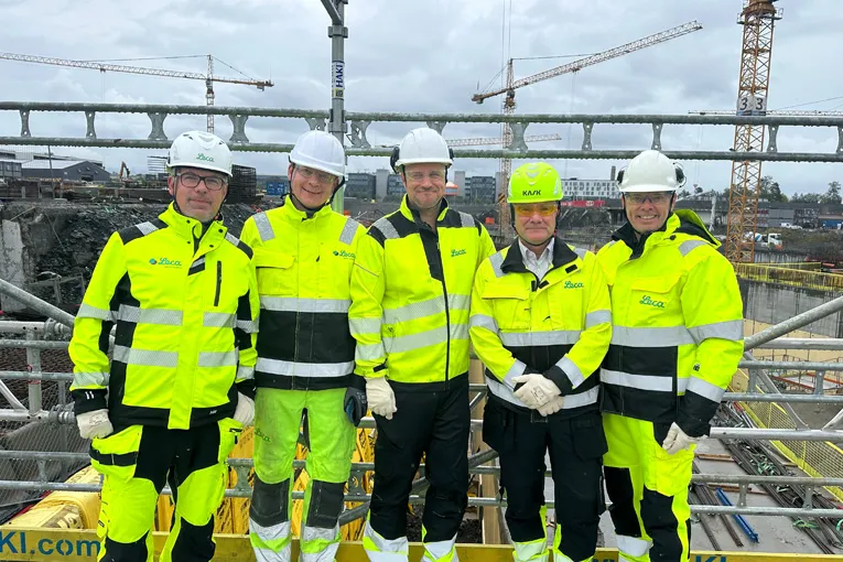 Fem representanter fra Leca og samarbeidspartnere står på byggeplassen foran Fornebubanen med kraner i bakgrunnen.
