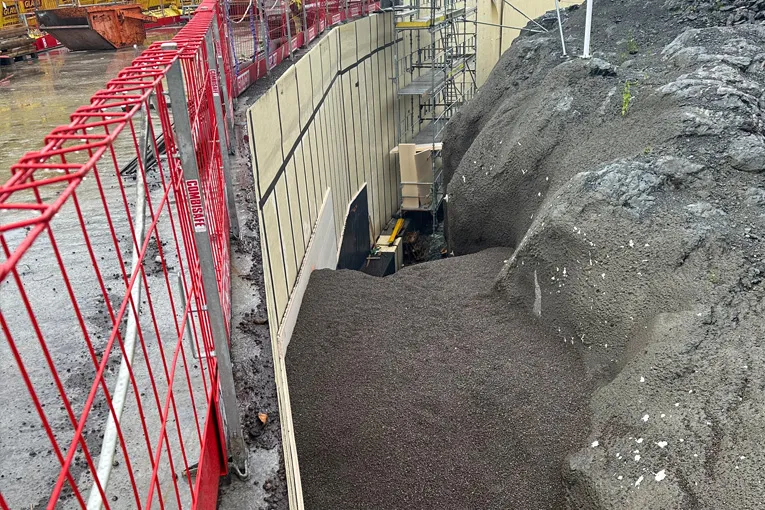 Grøft sett ovenfra der Leca® Lettklinker er fylt inn langs en betongvegg med stillaser og rød sikringsrist.