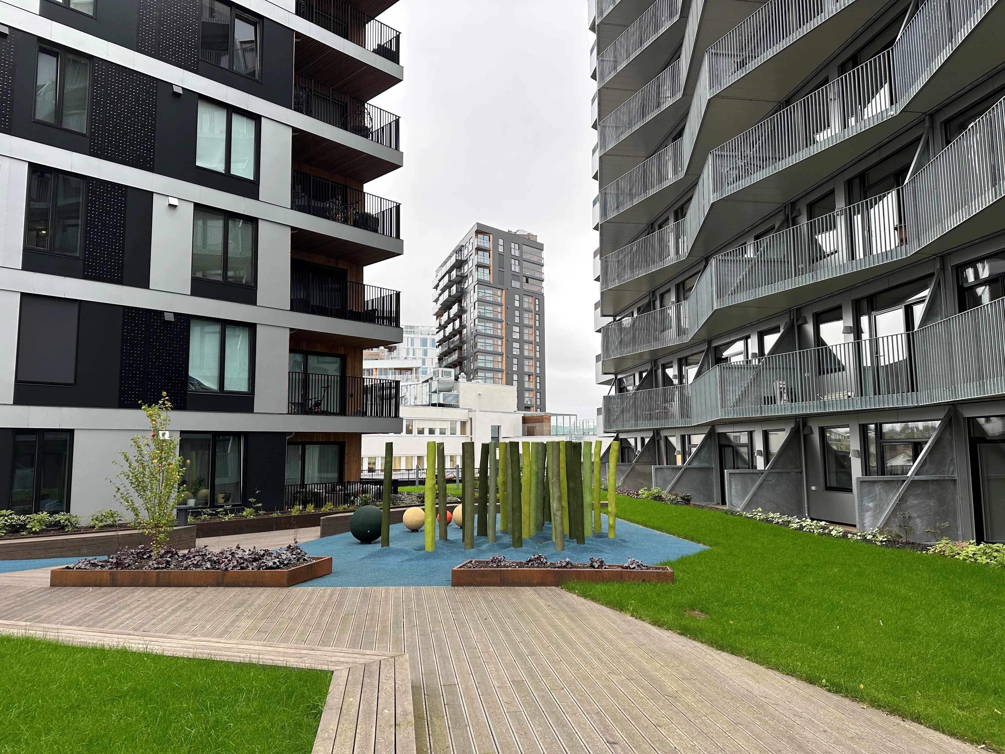 Felles tak- og gårdsrom mellom moderne boligbygg, med grønne flater, lekeelementer og bærekraftig uteopphold.