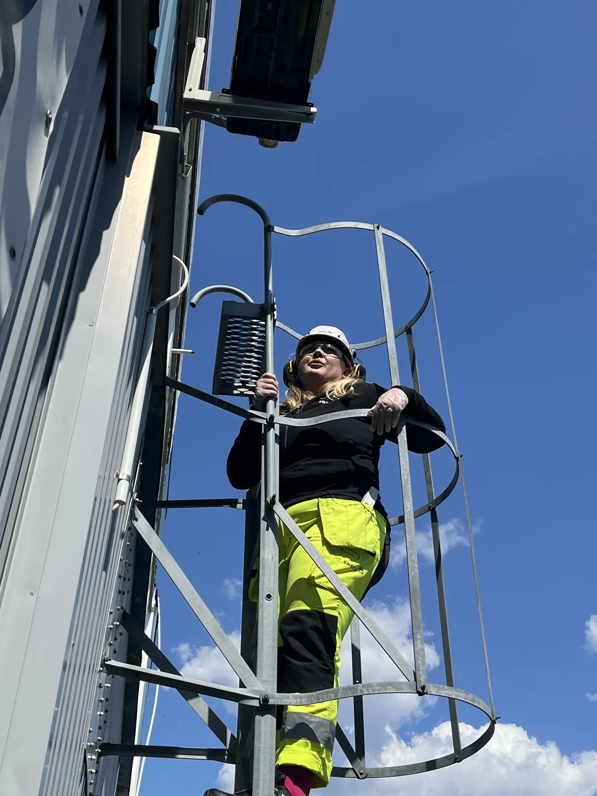 Amanda Borneke klatrer opp en metallstige iført hjelm, hørselsvern og gule vernebukser.