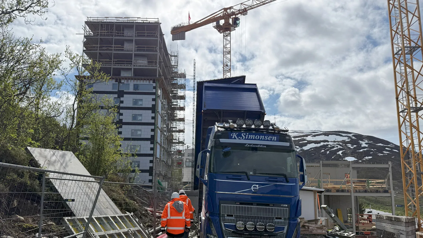 Blåsebil fra K. Simonsen AS klargjøres for levering av Leca® Lettklinker på byggeplassen i Øvre Kroken, med høye boligblokker og kraner i bakgrunnen.